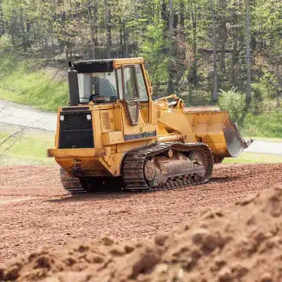 Photo shows tracked bulldozer leveling soil on construction site, operated by land clearing contractors