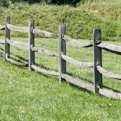 Weathered split-rail fence curves across grassy pasture, illustrating fence line clearing needs and upkeep tasks