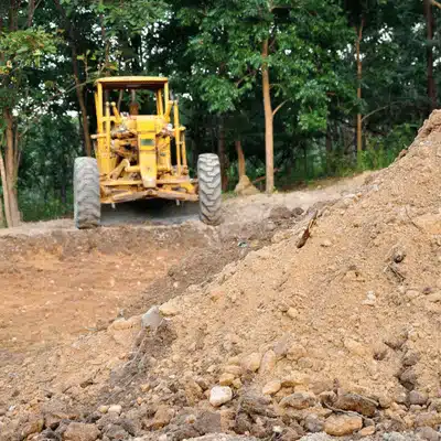 Construction vehicle prepares site by moving soil piles for precise grading and leveling across terrain