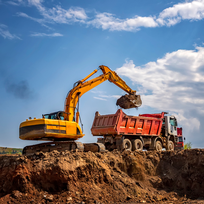 Yellow excavator loads soil into a red dump truck during construction excavation services on a worksite.