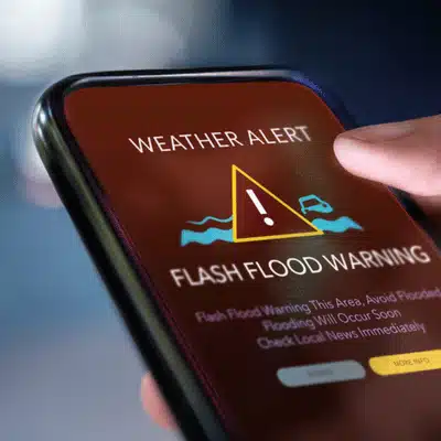 Finger taps phone displaying flash flood warning, urgent weather alert for nearby area and roads
