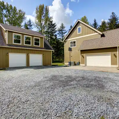 Two houses with garages showcasing different types of driveways on a spacious gravel area