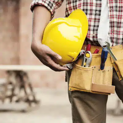 Close-up of tradesperson holding hard hat, tool belt stocked with tools at building site today