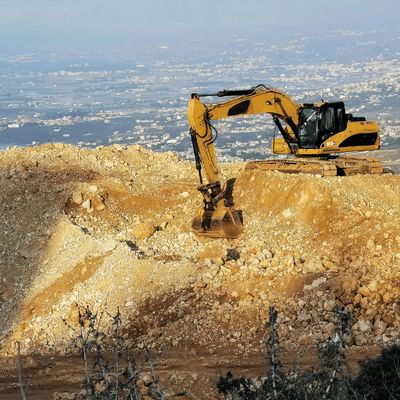 Large excavator works on rocky slope, moving earth for commercial excavation services near town below