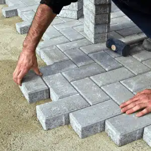 A contractor places interlocking pavers neatly into sand, offering an alternative to concrete driveway contractor work