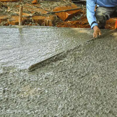 Worker levels freshly poured wet concrete slab using straightedge board, smoothing surface during driveway installation