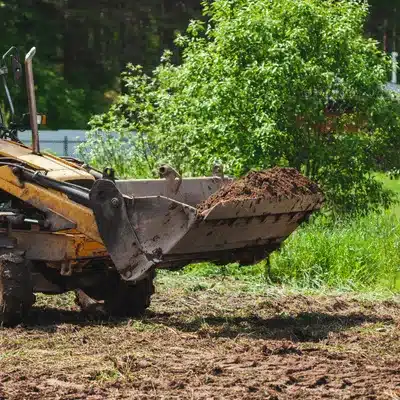 Photo shows loader bucket lifting dirt in grassy lot, used by land clearing contractors