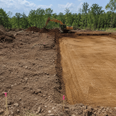 A grading and excavation site shows rough soil beside a smooth compacted pad ready for future construction.