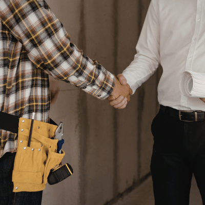 Contractor shakes client’s hand beside tool belt and plans, agreeing on commercial excavation services terms