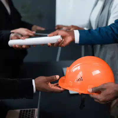 Contractors exchange blueprints and safety gear during a planning discussion for upcoming construction work