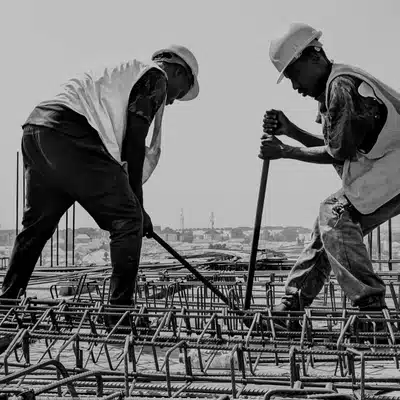 Two laborers compact rebar framework after concrete removal, using rods on elevated construction deck safely