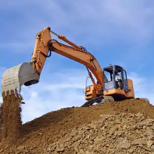 Excavator dumps rocky soil from slope, emphasizing terrain difficulty and its effect on excavation cost