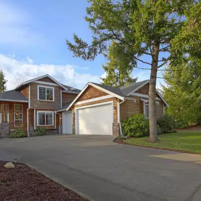 Modern suburban home with white garage door, concrete driveway, and landscaped yard with tall trees
